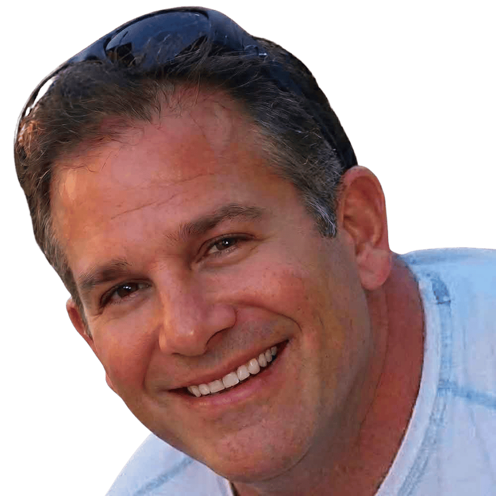 Smiling man with sunglasses outdoors, sunny day, casual attire.